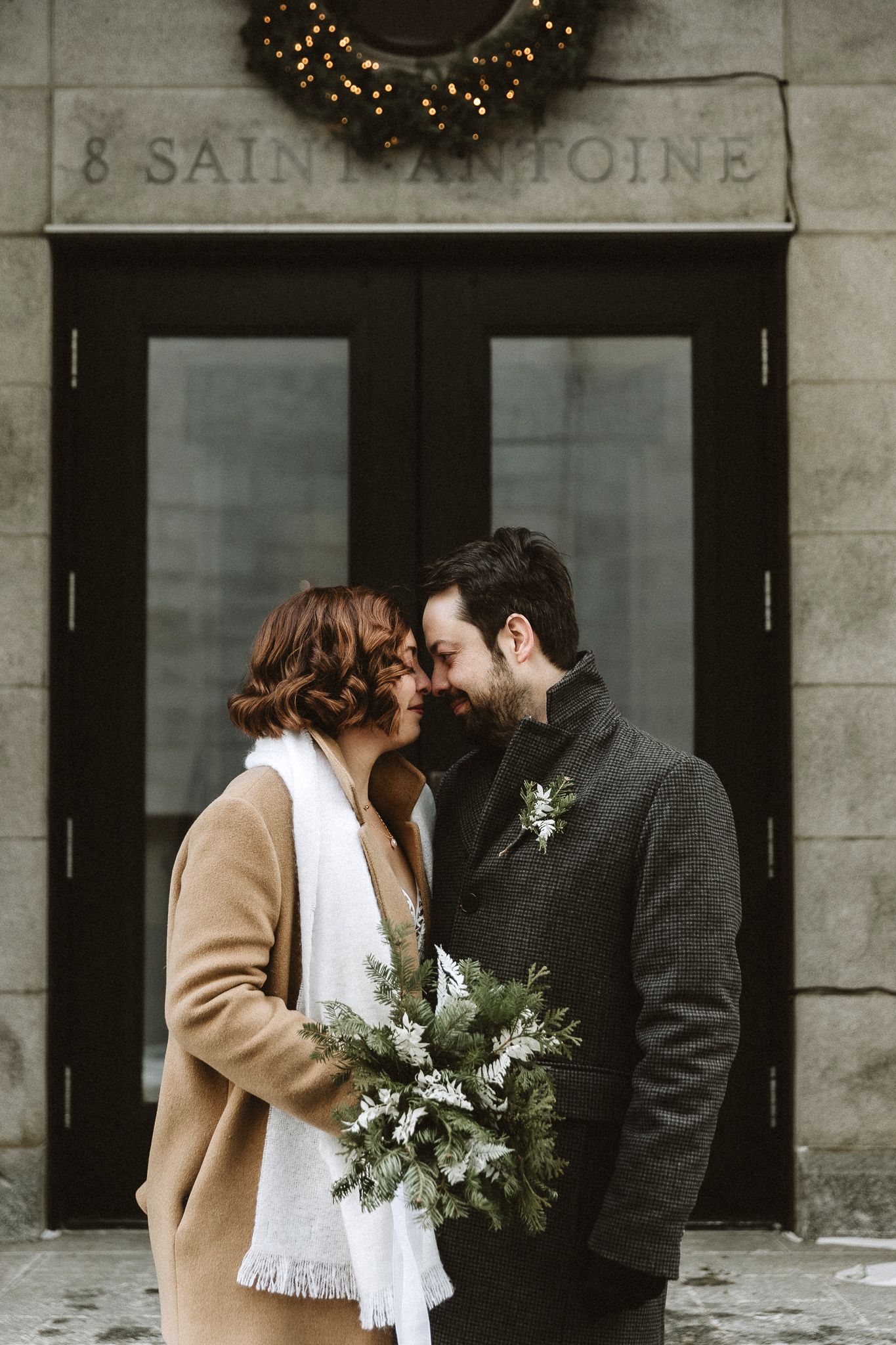 A winter wedding portrait in front of stone building entrance with holiday wreath decoration.