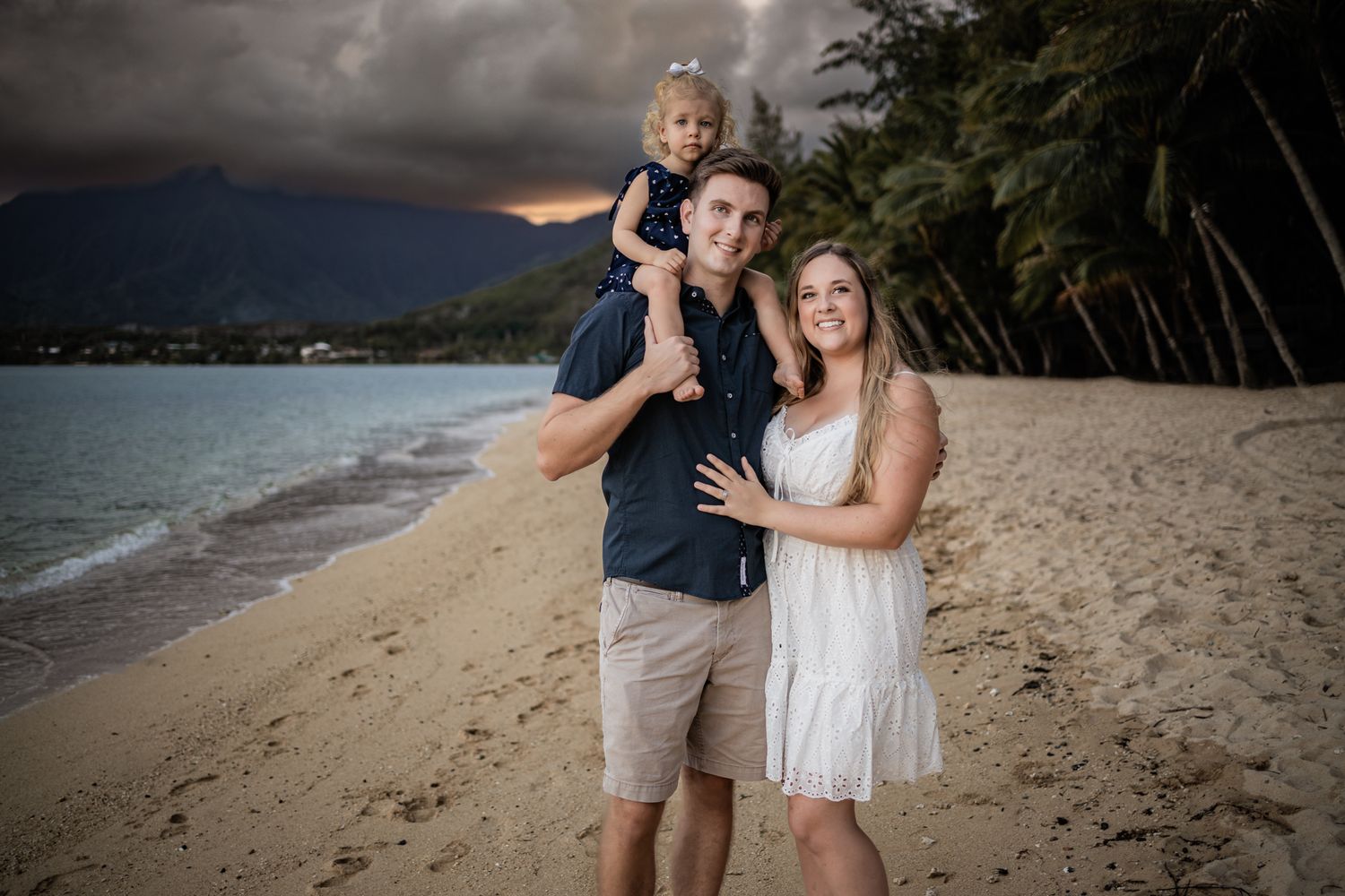 Family portrait at sunset on a Hawaiian beach with mountains and stormy skies in the background.