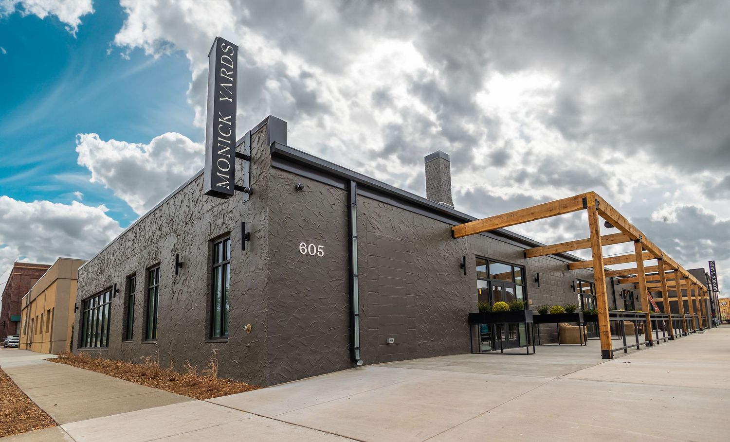 Industrial-style brick building with modern wooden pergola structure along sidewalk.