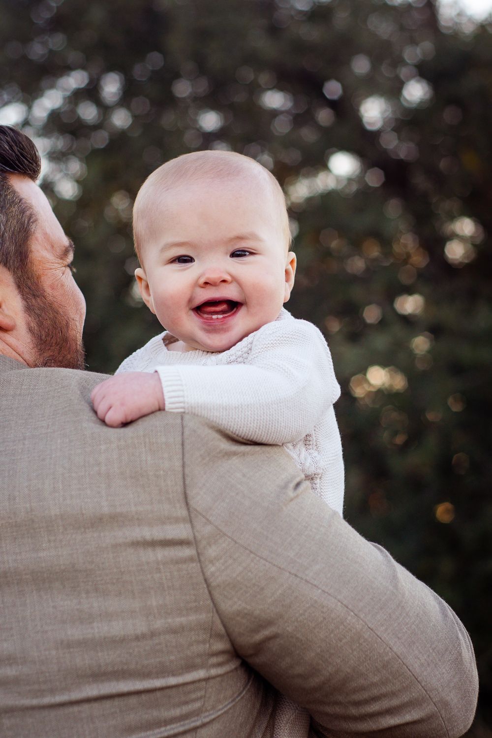 Happy baby in white sweater looking over shoulder while being held.