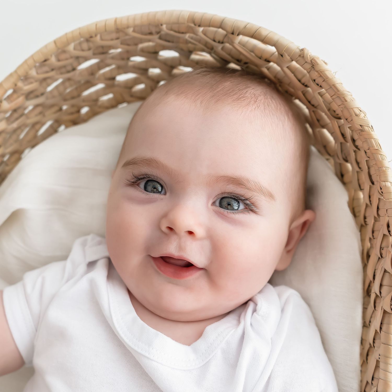 Baby wearing white outfit lies in woven basket with soft lighting.