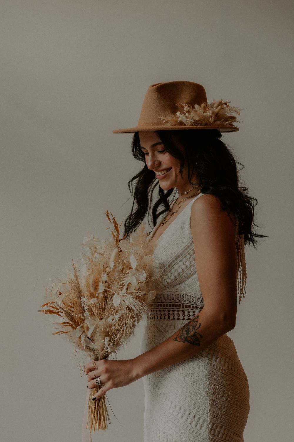 Bridal portrait featuring white fitted dress, dried floral bouquet and brown wide-brim hat.