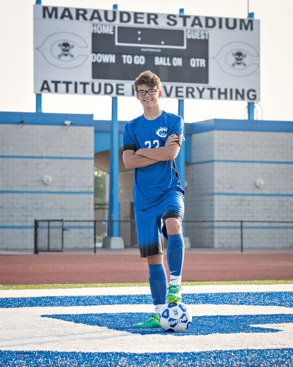 Male soccer player in blue jersey posing with ball at Marauder Stadium turf field.