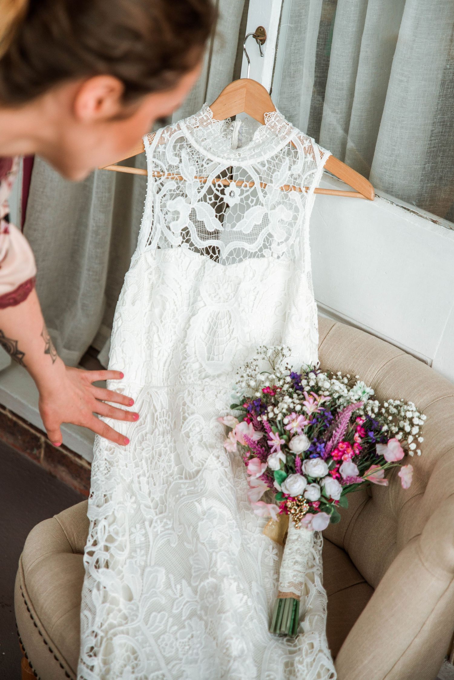 Detailed lace wedding dress hanging on display next to a colorful floral bouquet.
