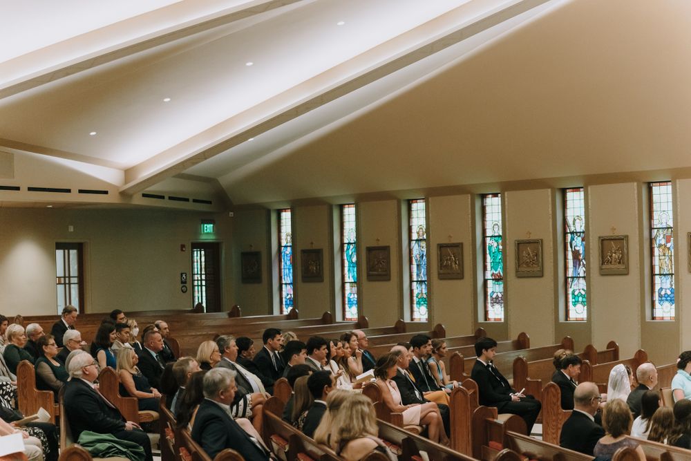 Interior view of wedding ceremony with guests seated in wooden pews of modern church.
