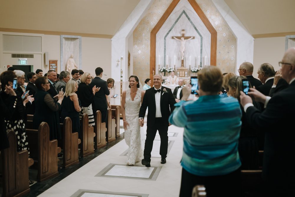 Wedding ceremony recessional in a small chapel with guests taking photos.