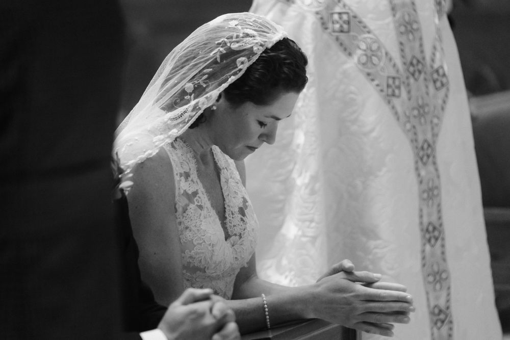 Bride in white lace dress standing in the rain under umbrellas with wedding party.