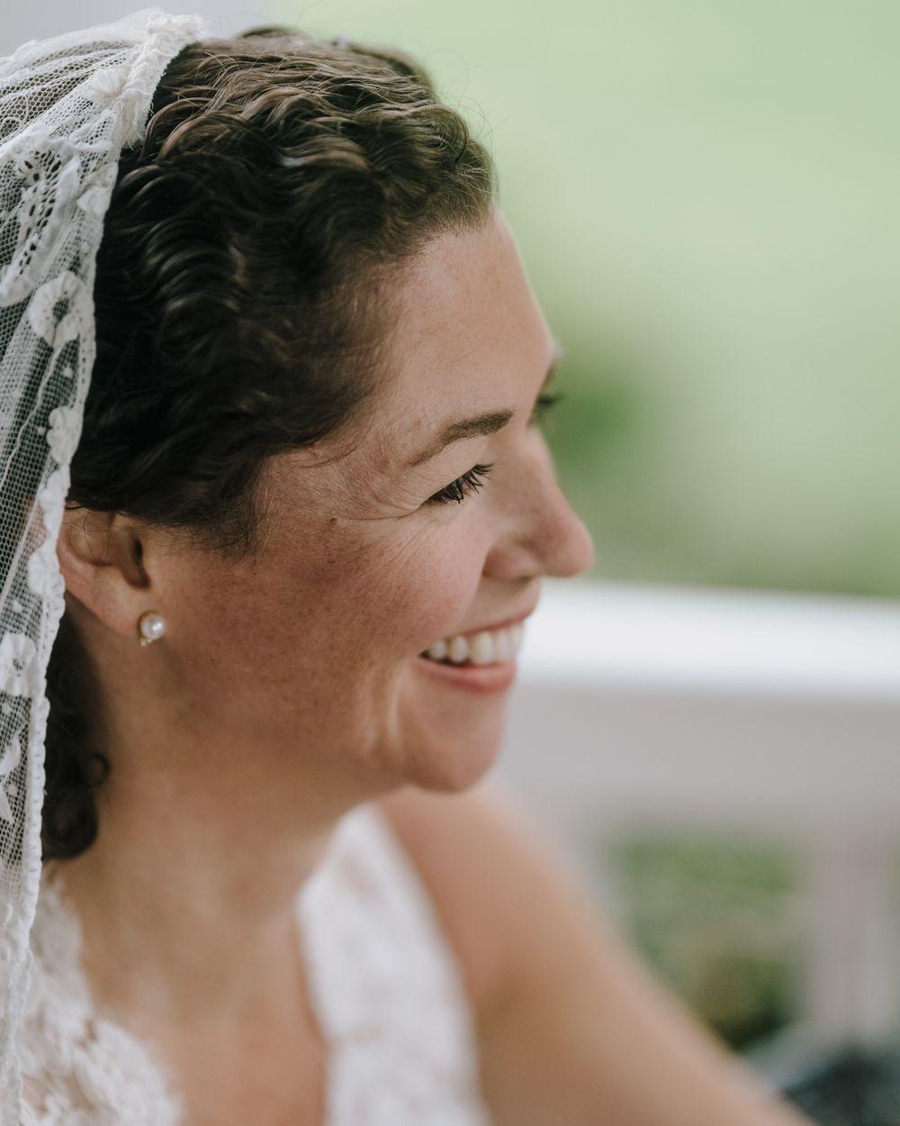 Close up profile of smiling bride wearing lace veil and pearl earrings.