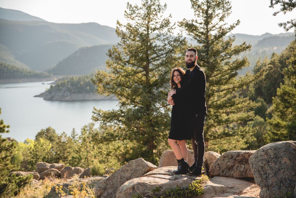 Couple enjoying scenic mountain lake views while standing on rocky overlook during sunset.