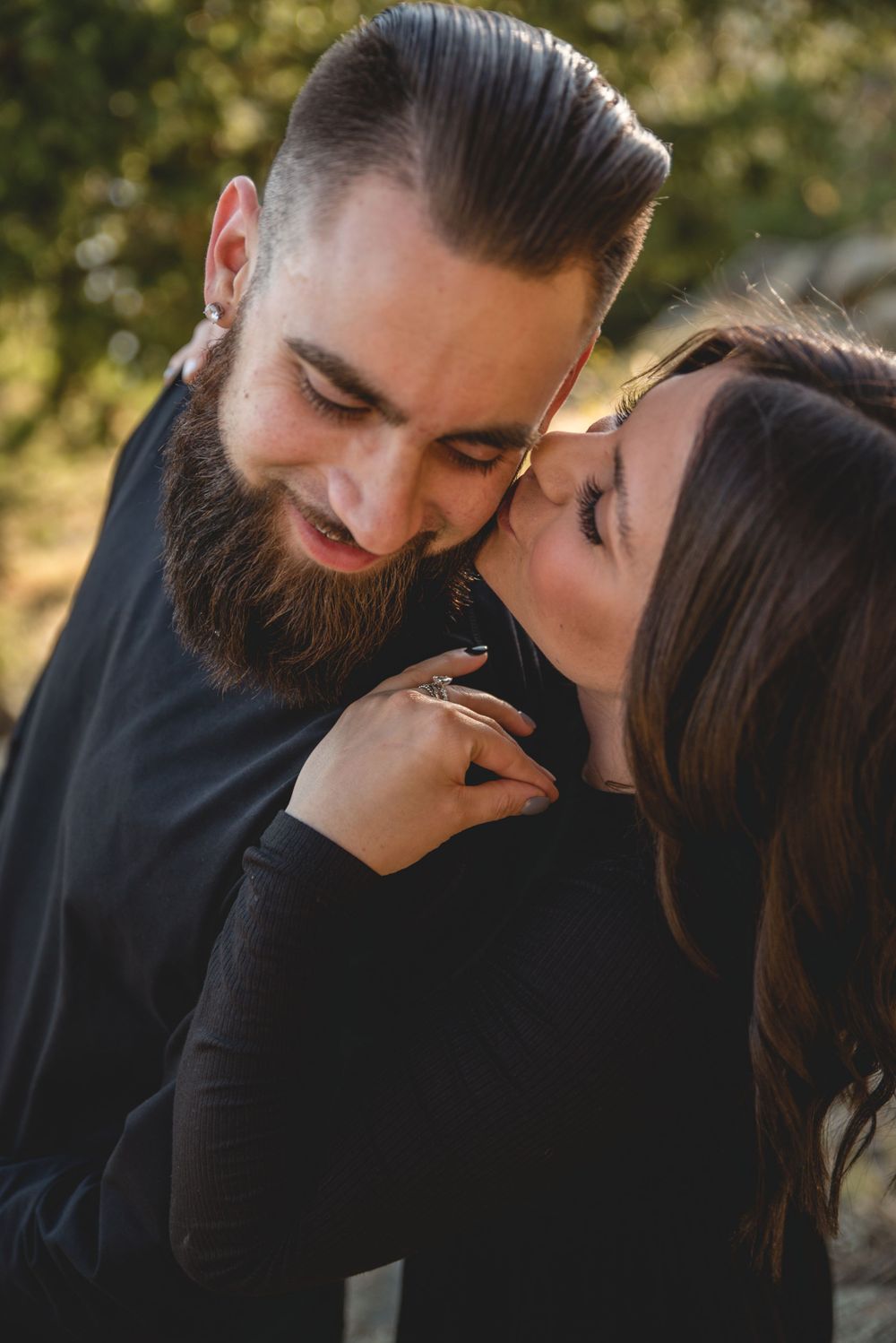 Romantic couple in black sharing an intimate moment outdoors with natural lighting.