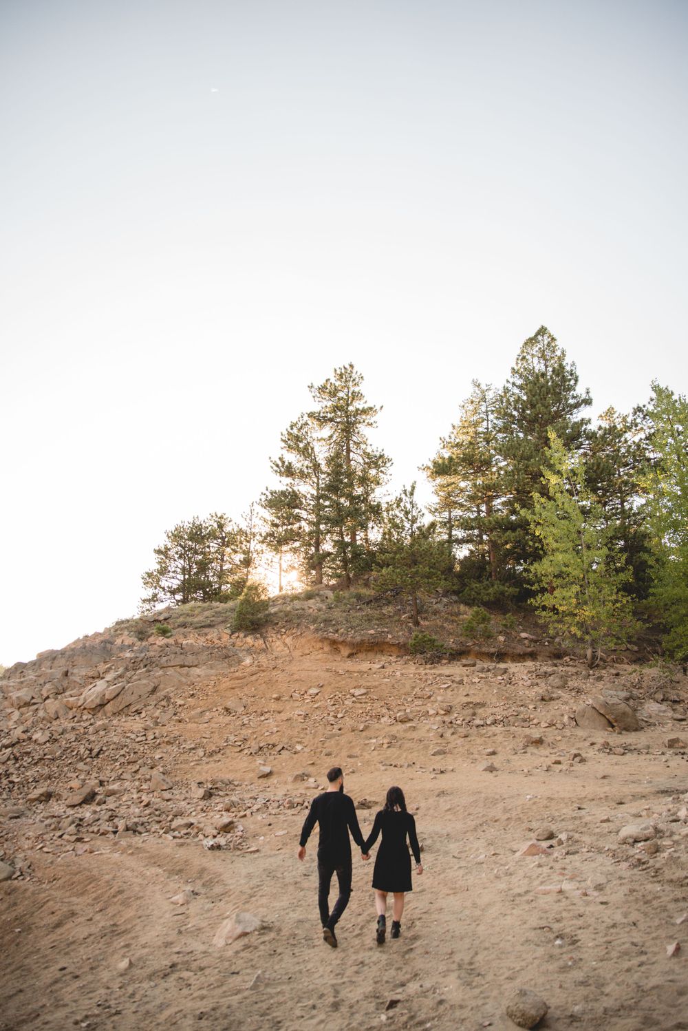 Silhouetted couple walking down rocky hillside during golden hour.
