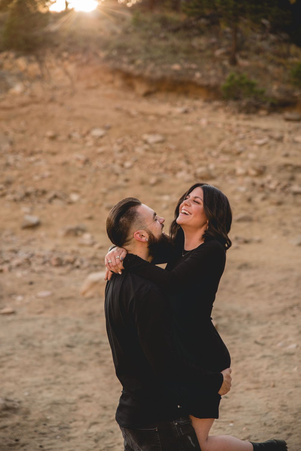 Couple embracing and laughing on rocky terrain during golden hour.