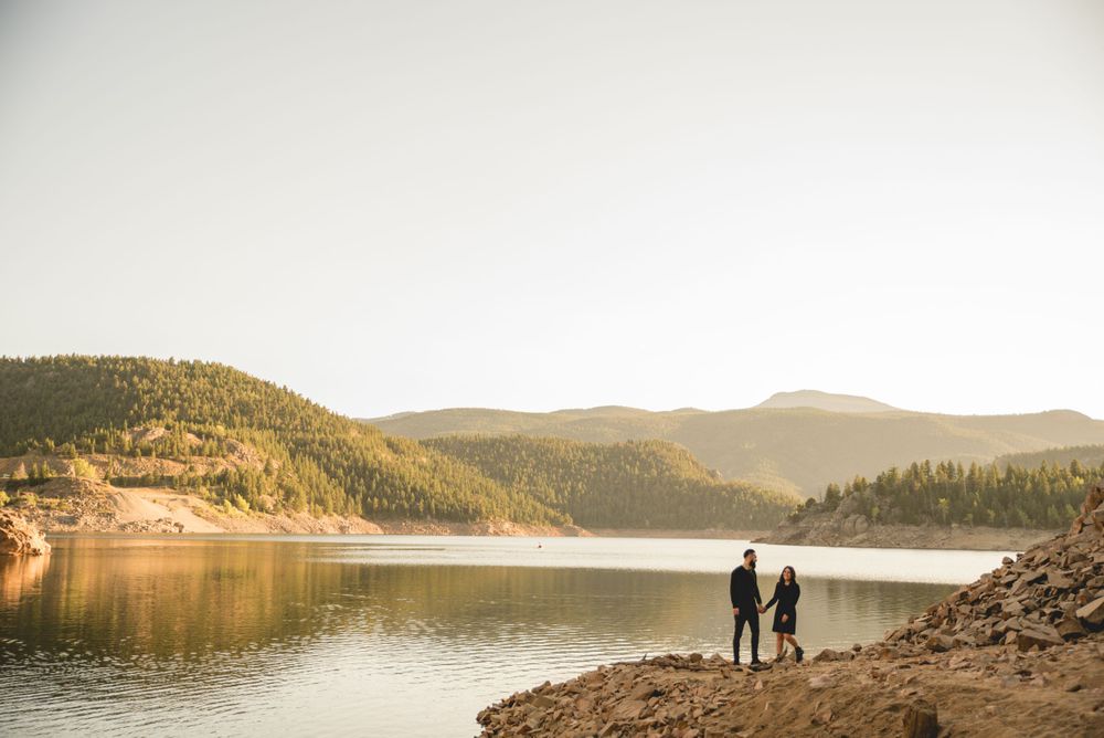 Two figures standing by mountain lake at sunset with scenic mountain backdrop.