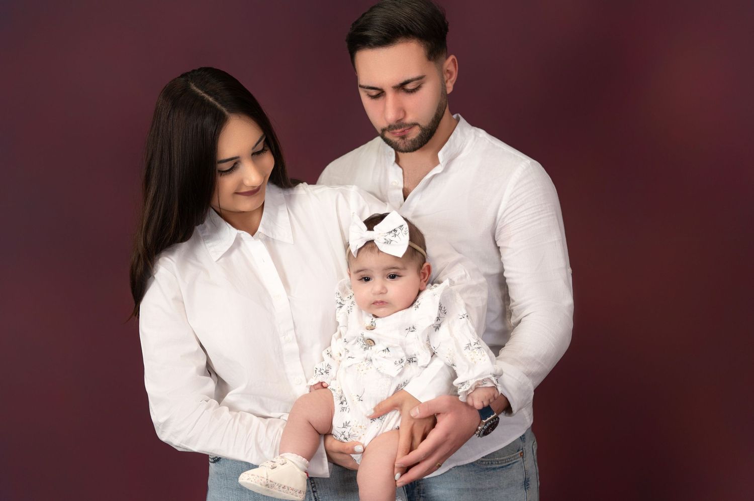 Family portrait session in formal attire against burgundy backdrop.