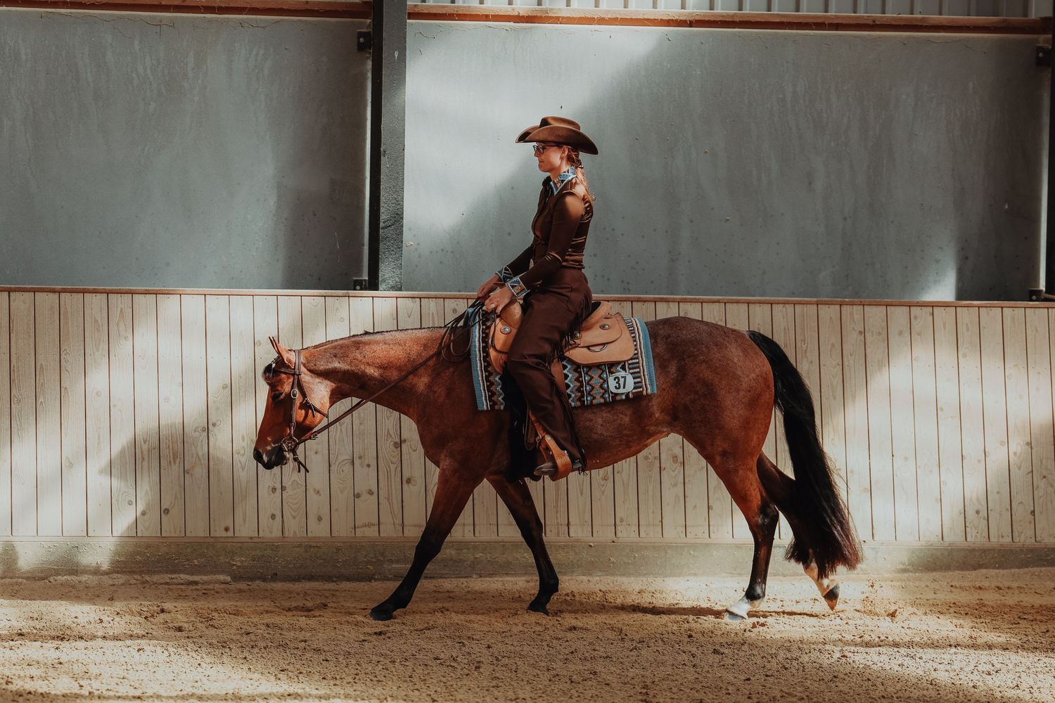 Horse and rider perform a western riding pattern against an indoor arena wall.