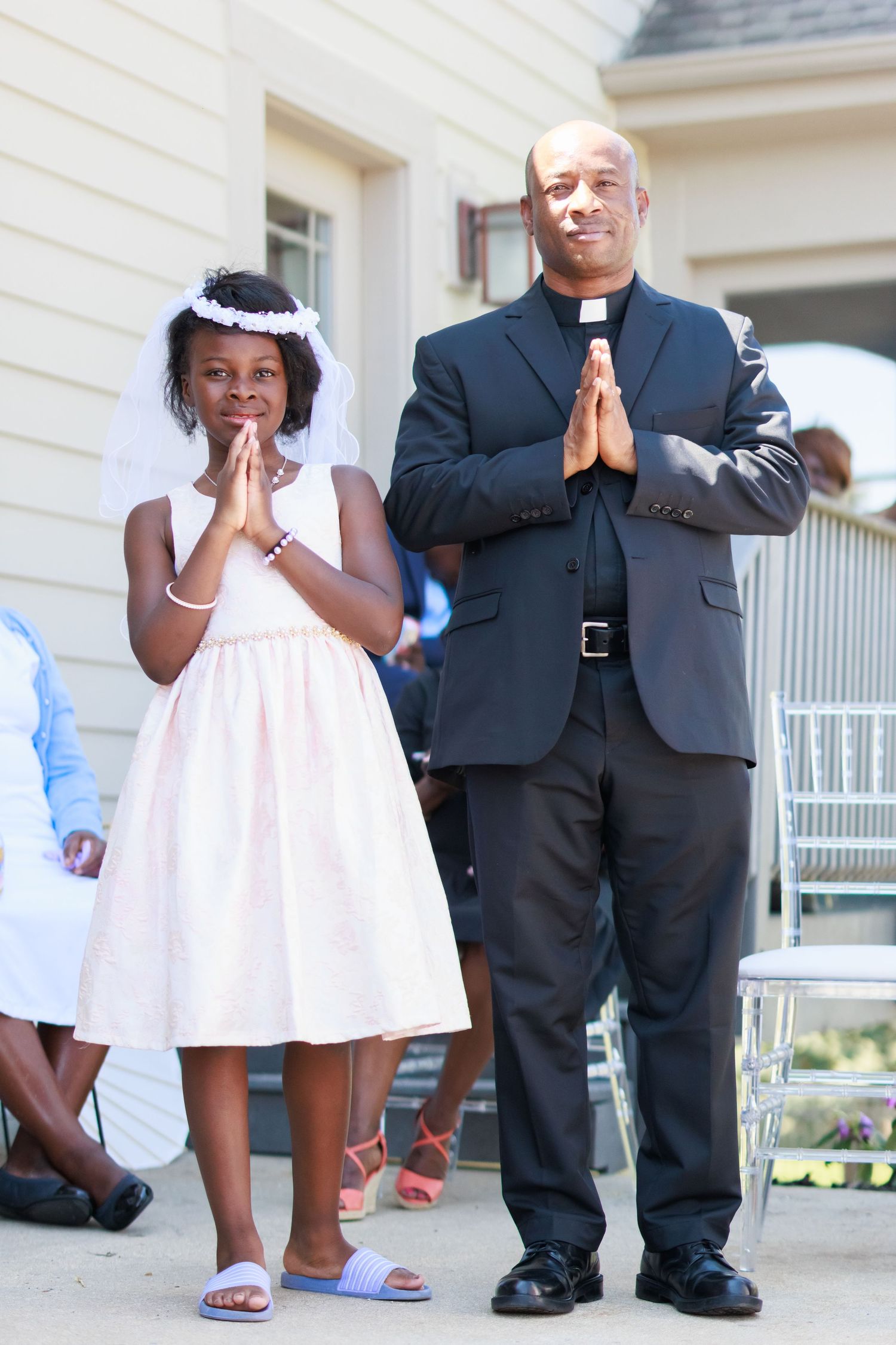 Father and daughter in formal attire praying together outside a white house.