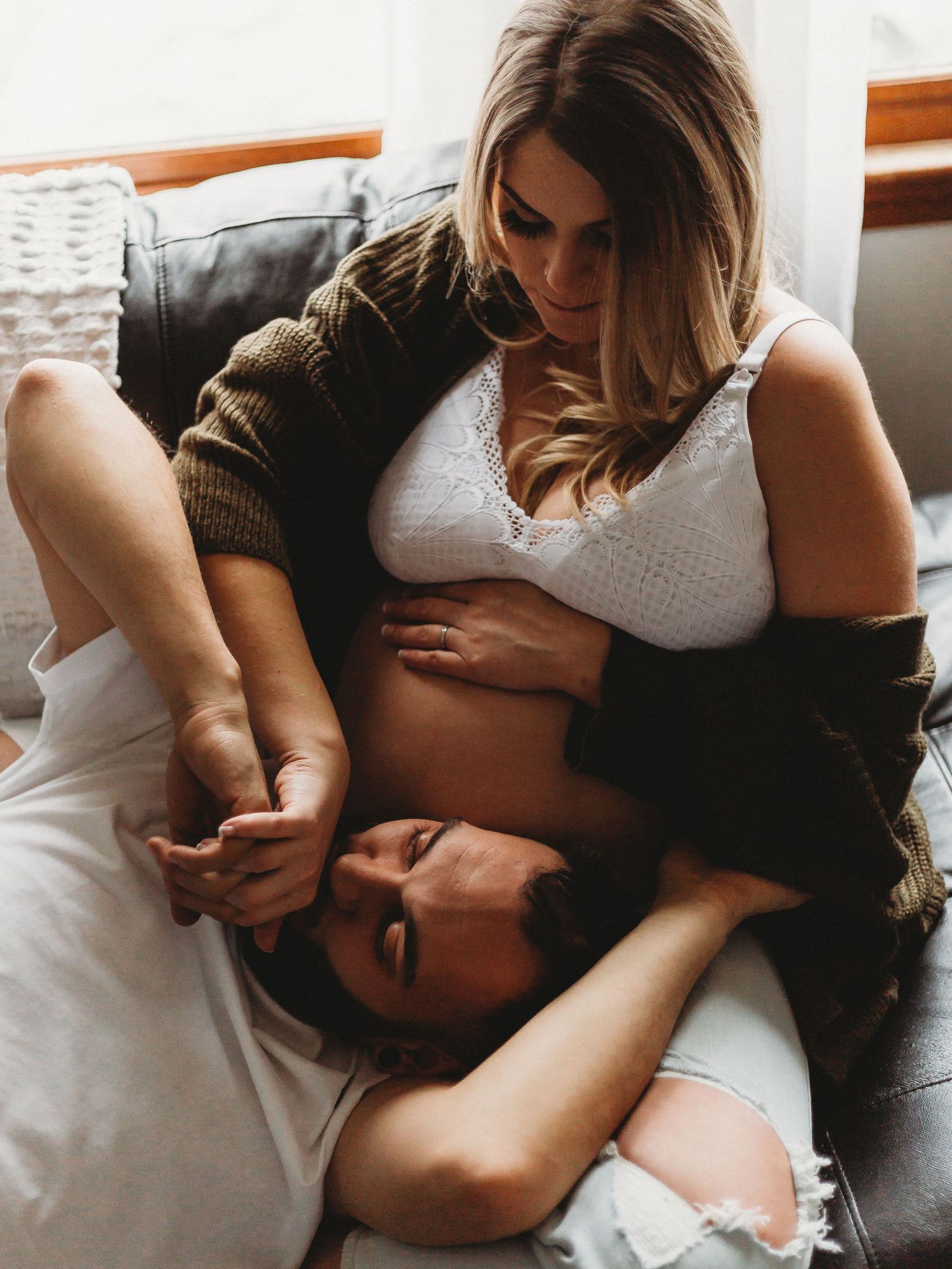 Intimate couple portrait in casual white clothing on grey couch.