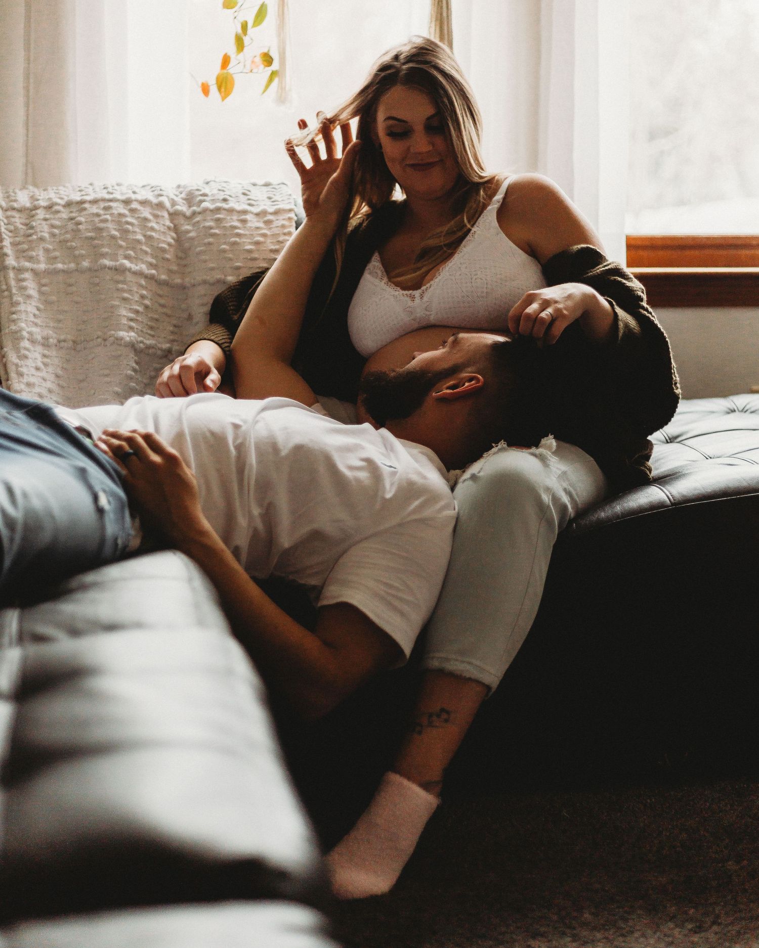Candid moment of a couple playfully interacting on a sofa by a window.