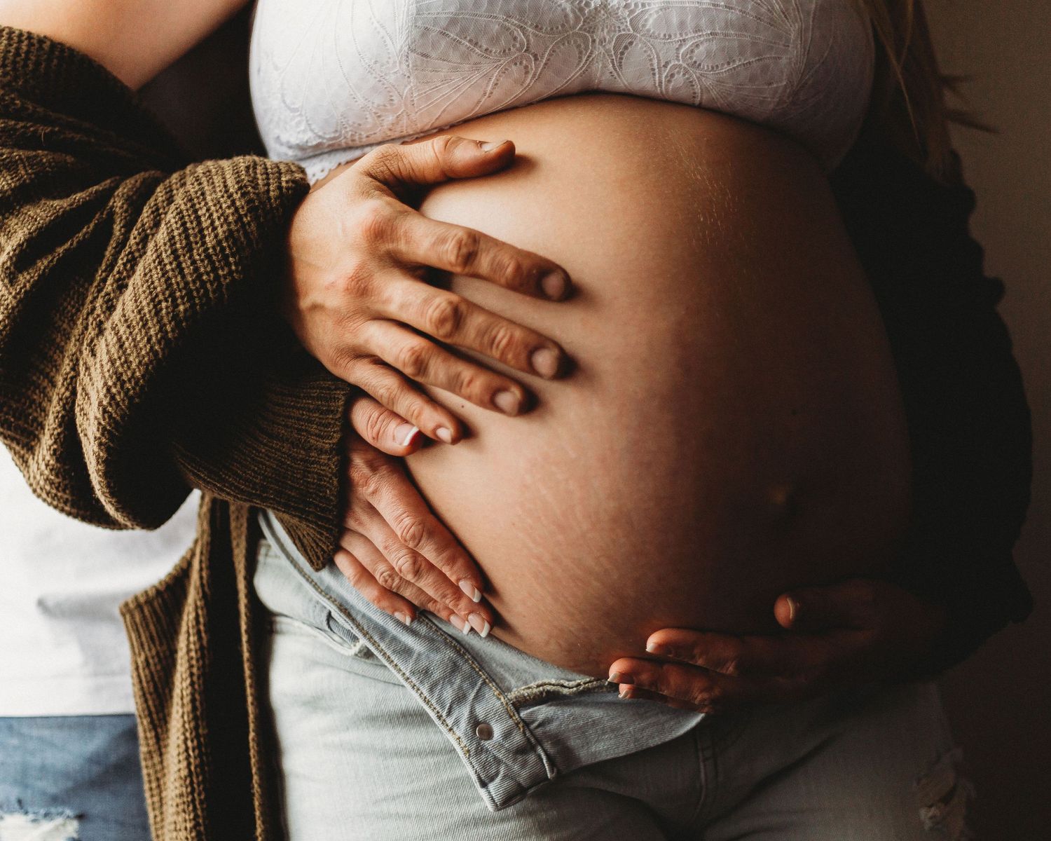 Close-up of hands gently cradling a pregnant belly in warm lighting.