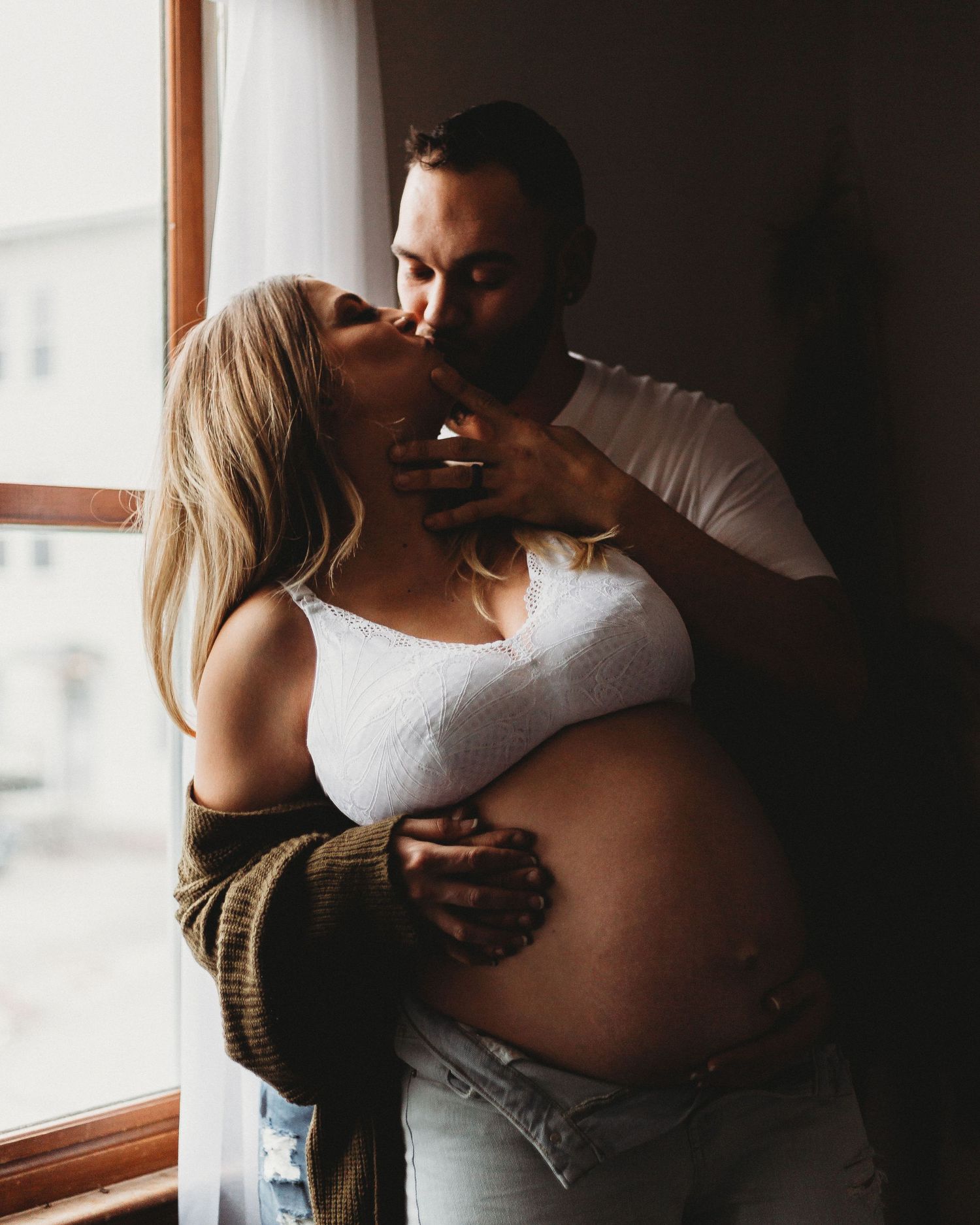 Intimate maternity photo of couple embracing near a window.
