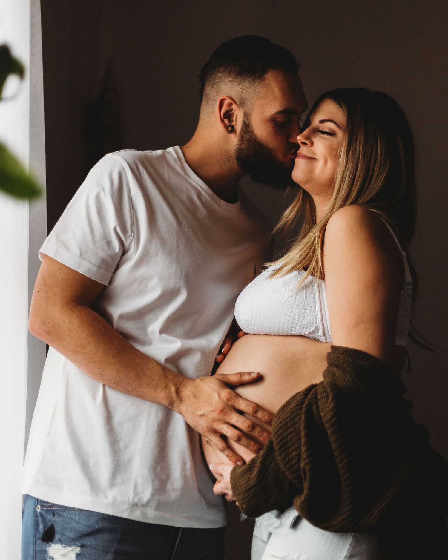 Sweet maternity moment captured as couple shares loving embrace by window.