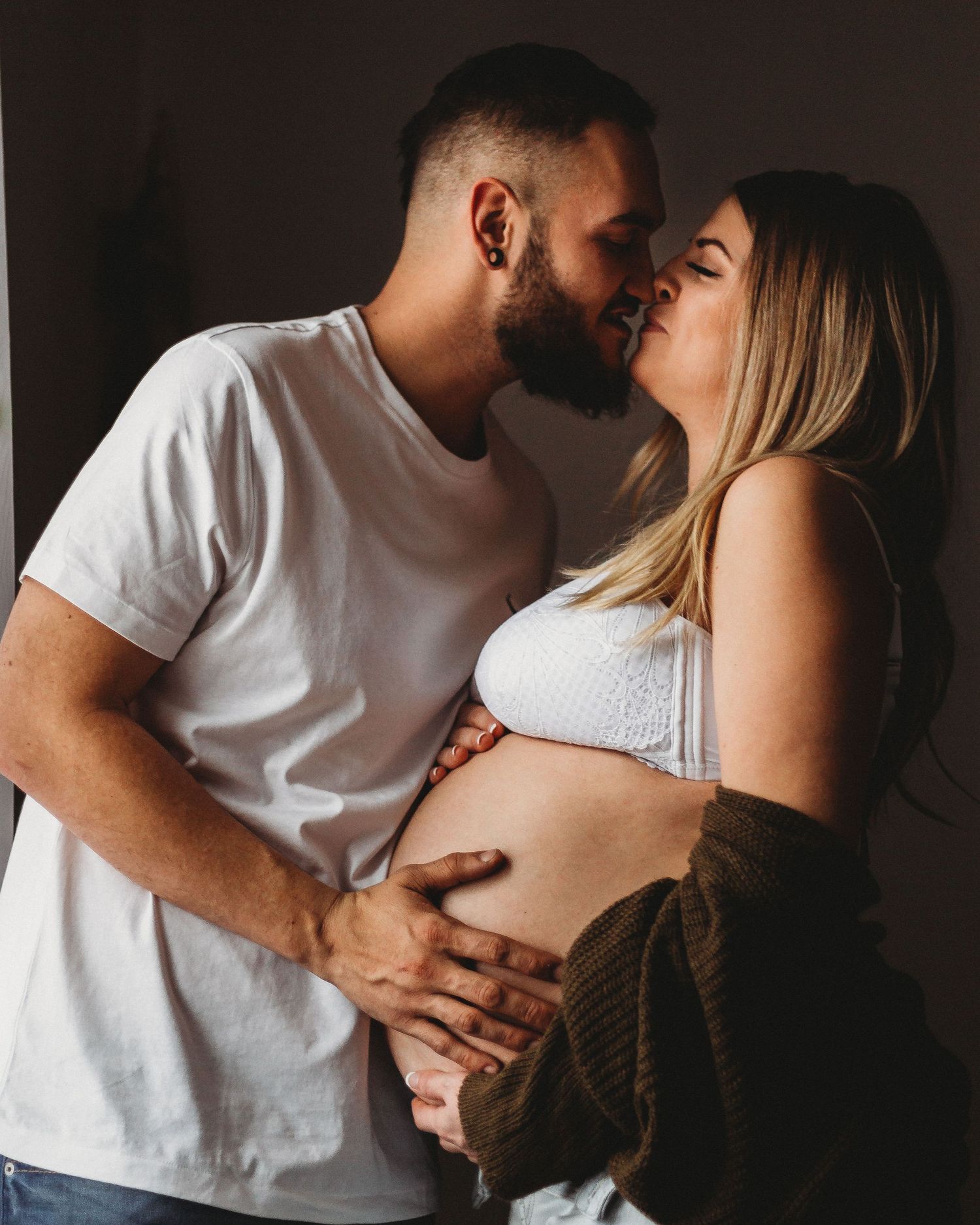 Romantic maternity photoshoot showing couple's affection in moody lighting.