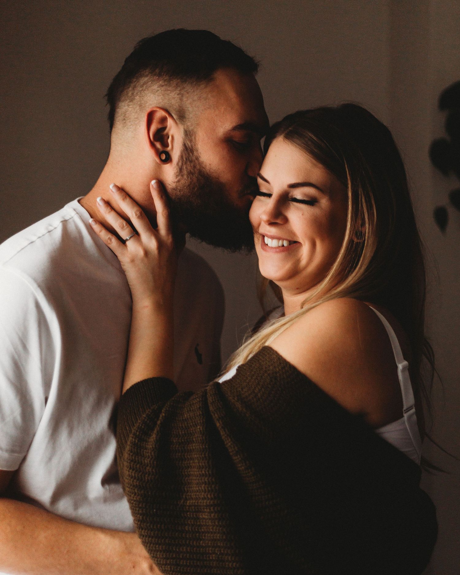 Intimate couple sharing a tender moment while smiling and embracing in natural lighting.