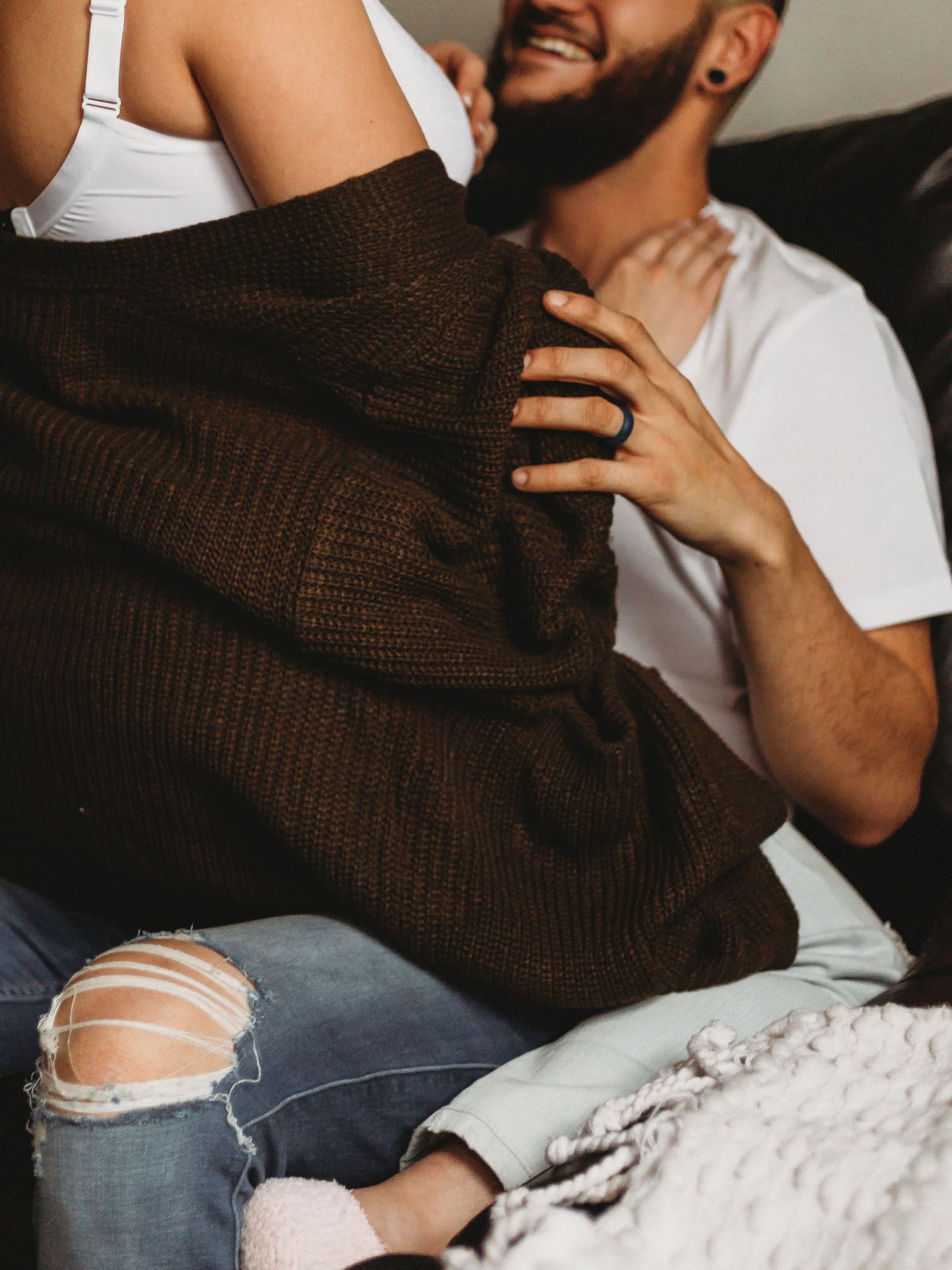 Close up of couple on couch with focus on brown sweater and ripped jeans details.