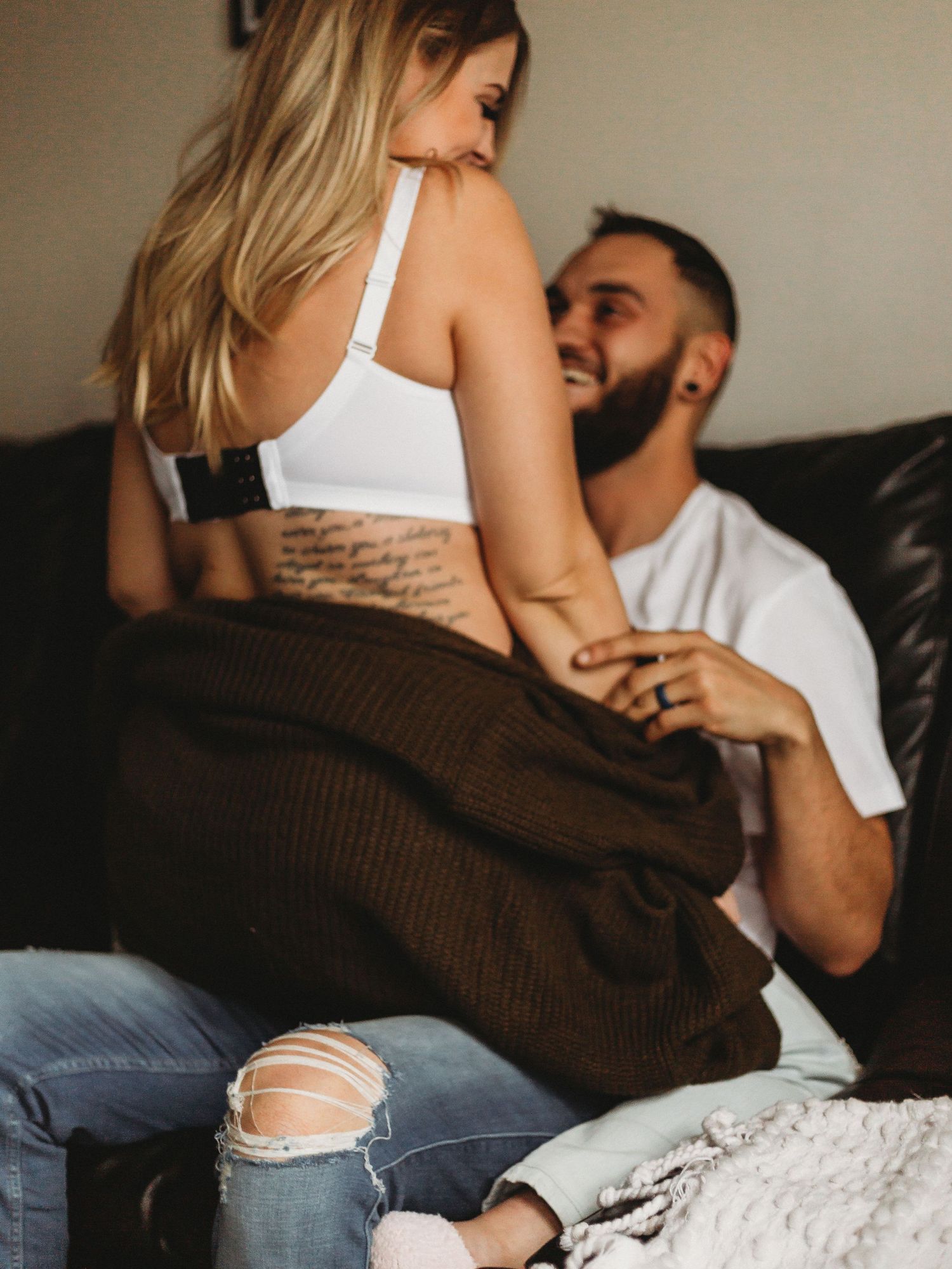 Intimate couple moment on leather couch with focus on casual clothing and tattoo details.