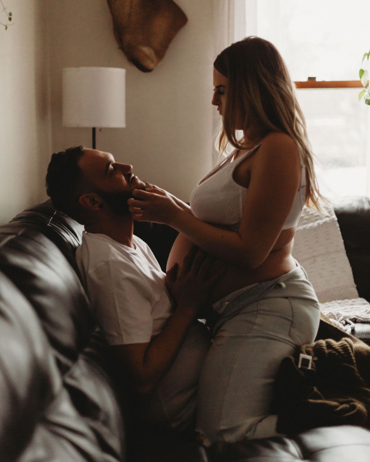 Artistic maternity photo capturing couple's playful interaction on couch.