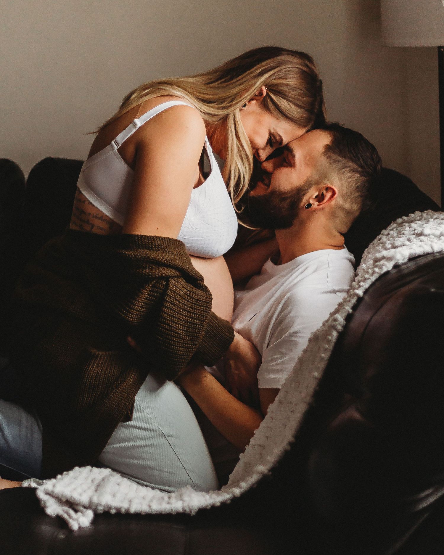 Intimate couple sharing a tender moment together on a dark leather couch with a brown cardigan and white top.