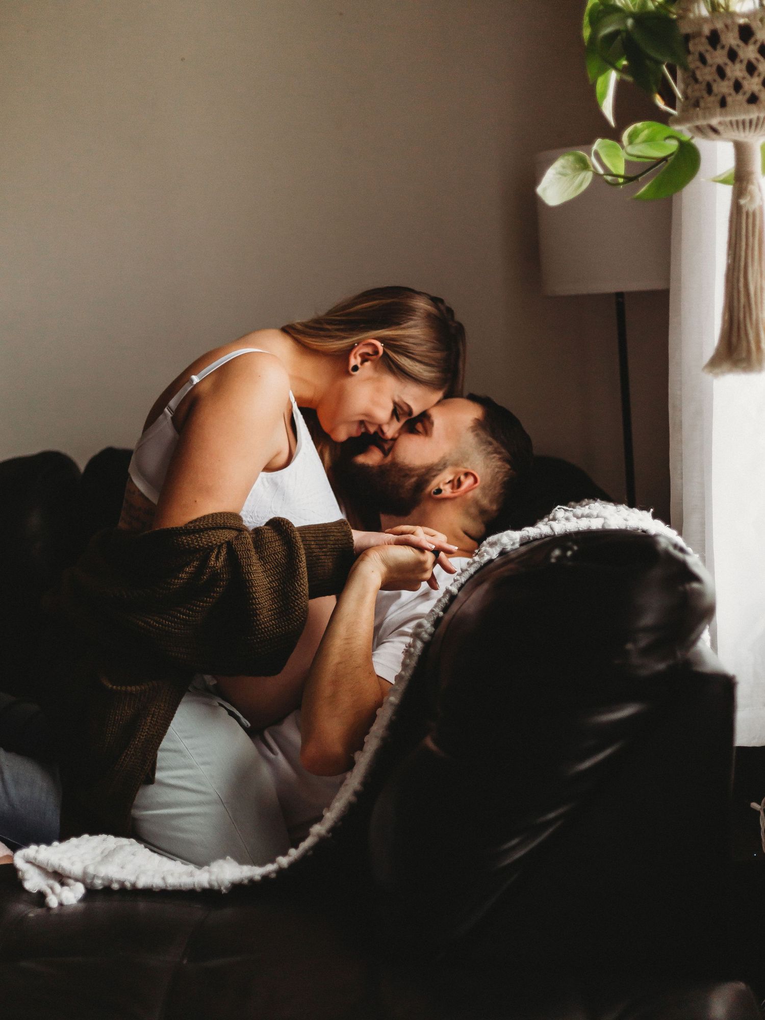 Warm and intimate moment between couple lounging on leather sofa with decorative plant in background.