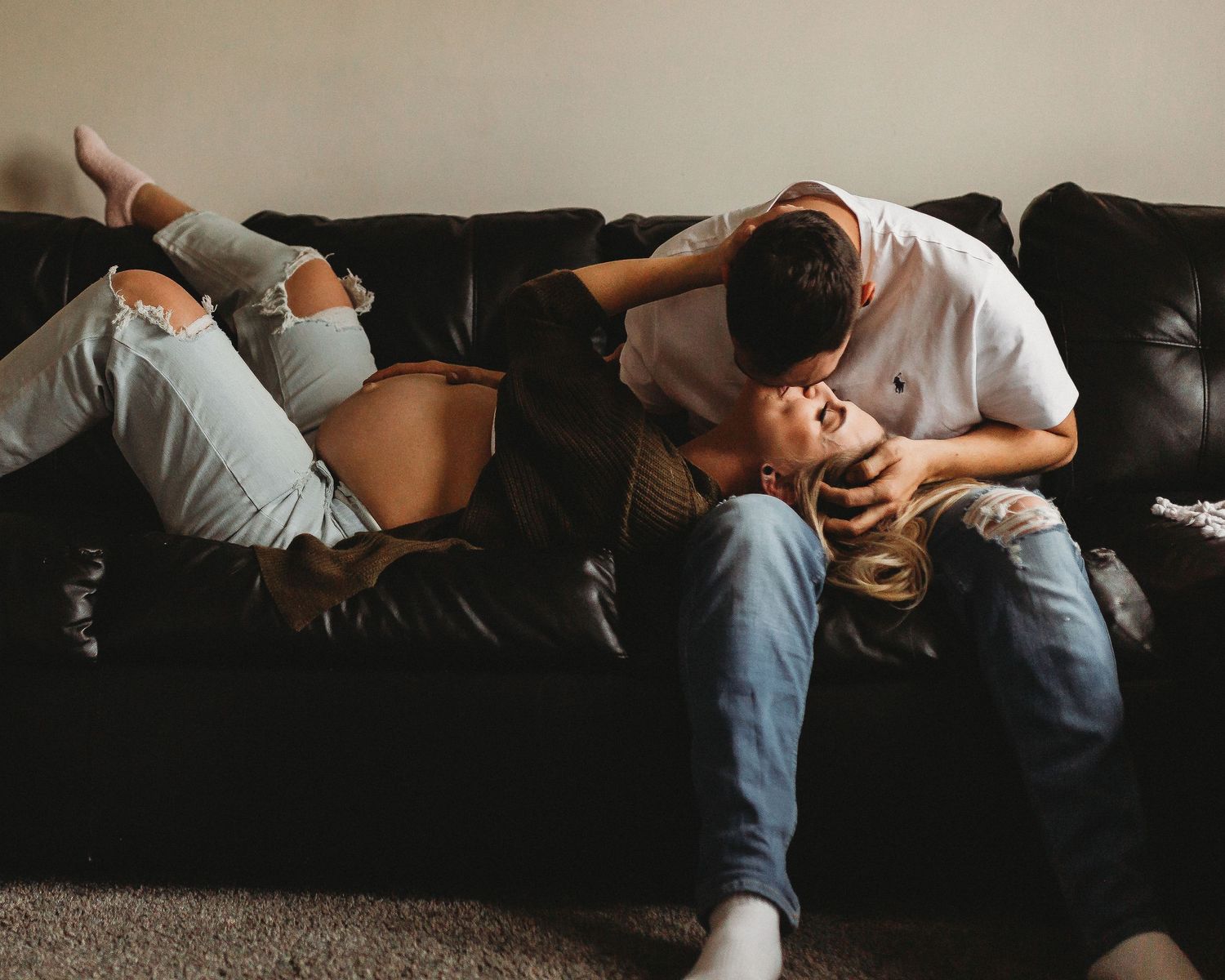 Couple in casual attire sharing intimate moment on dark leather couch.