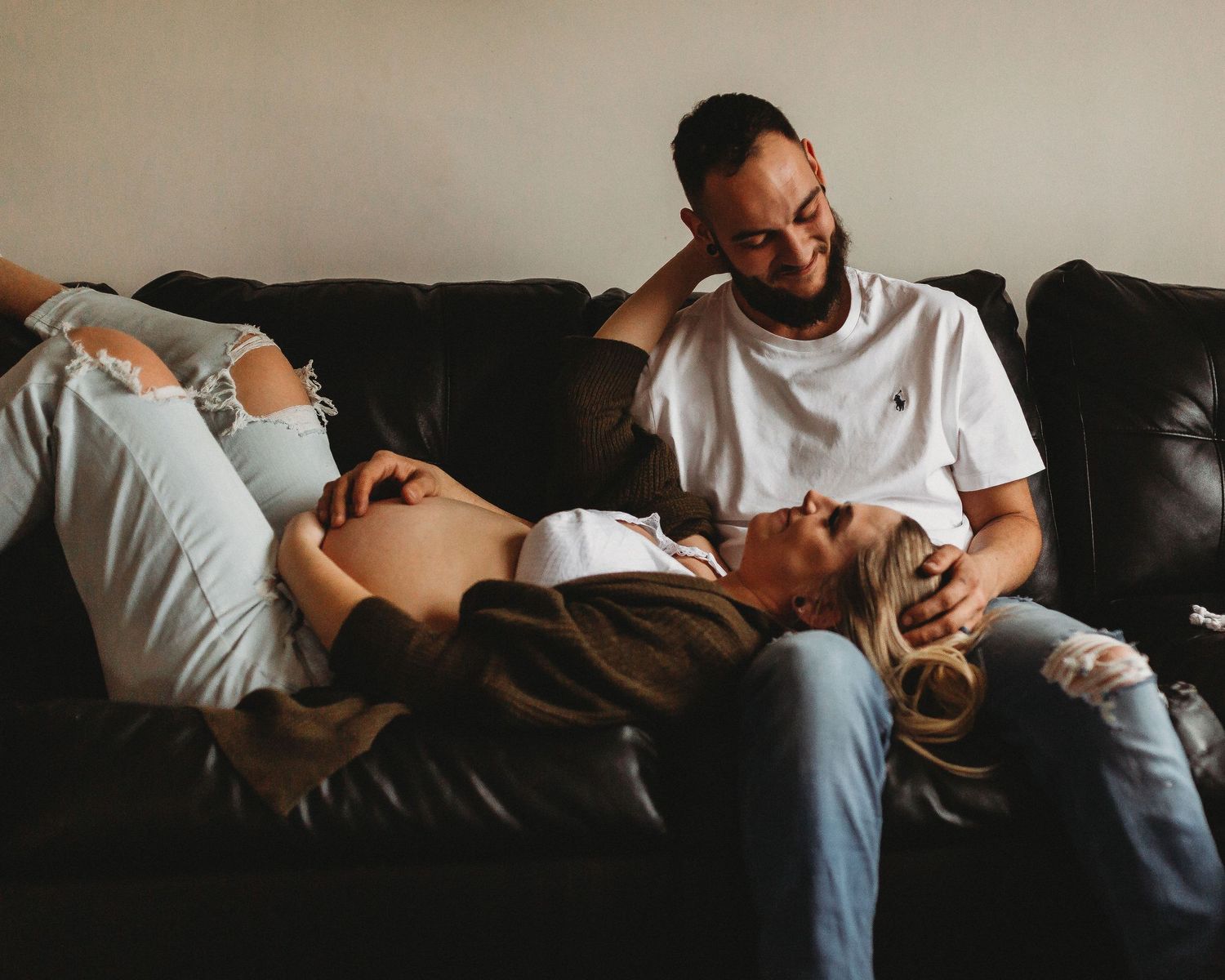 Couple enjoying tender moment while lounging together on dark leather sofa.