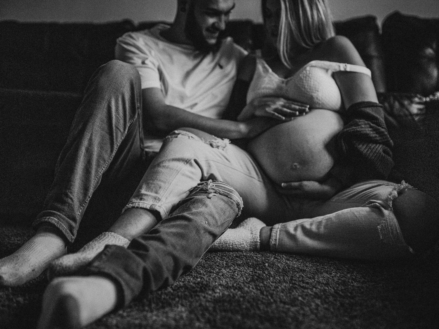 Black and white maternity photo showing couple's tender moment on couch.