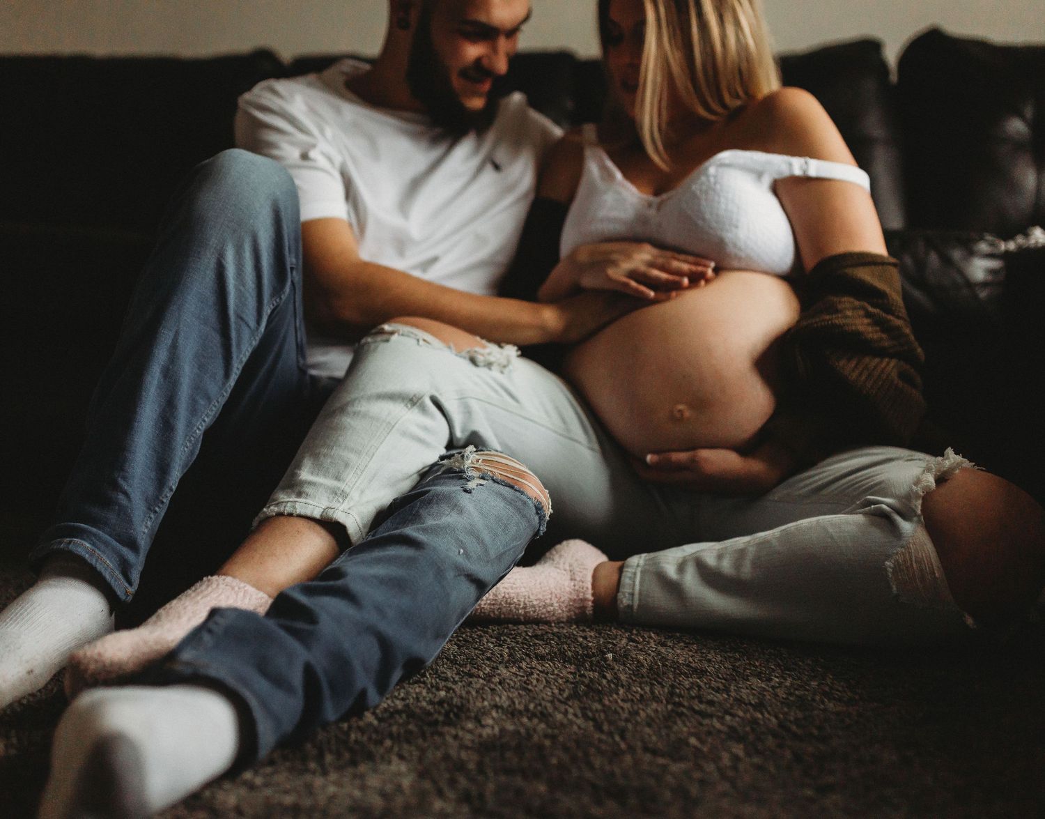Intimate pregnancy photo with couple relaxing on dark leather couch.