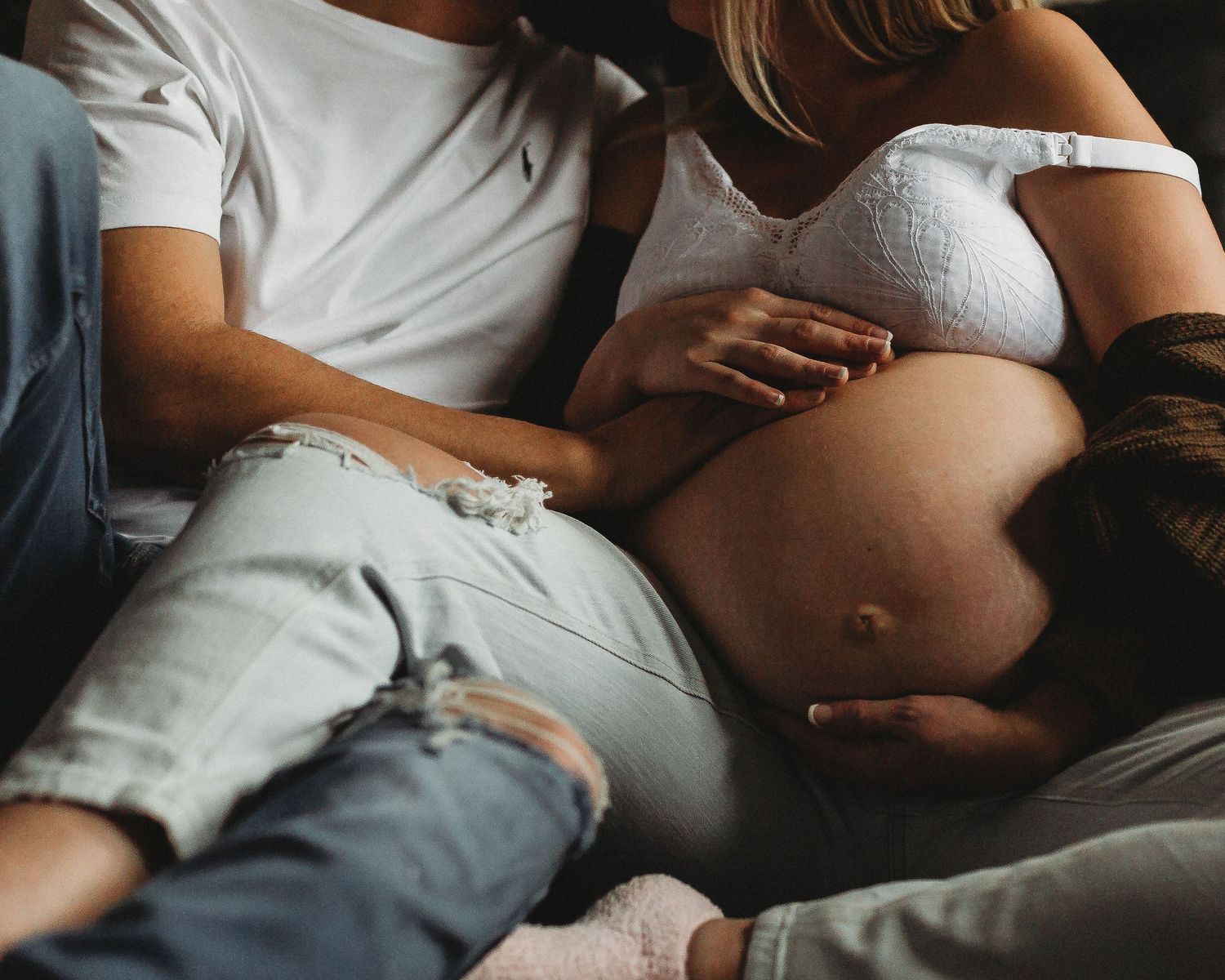 Intimate maternity photo of couple lying together on a bed as they embrace a pregnant belly.