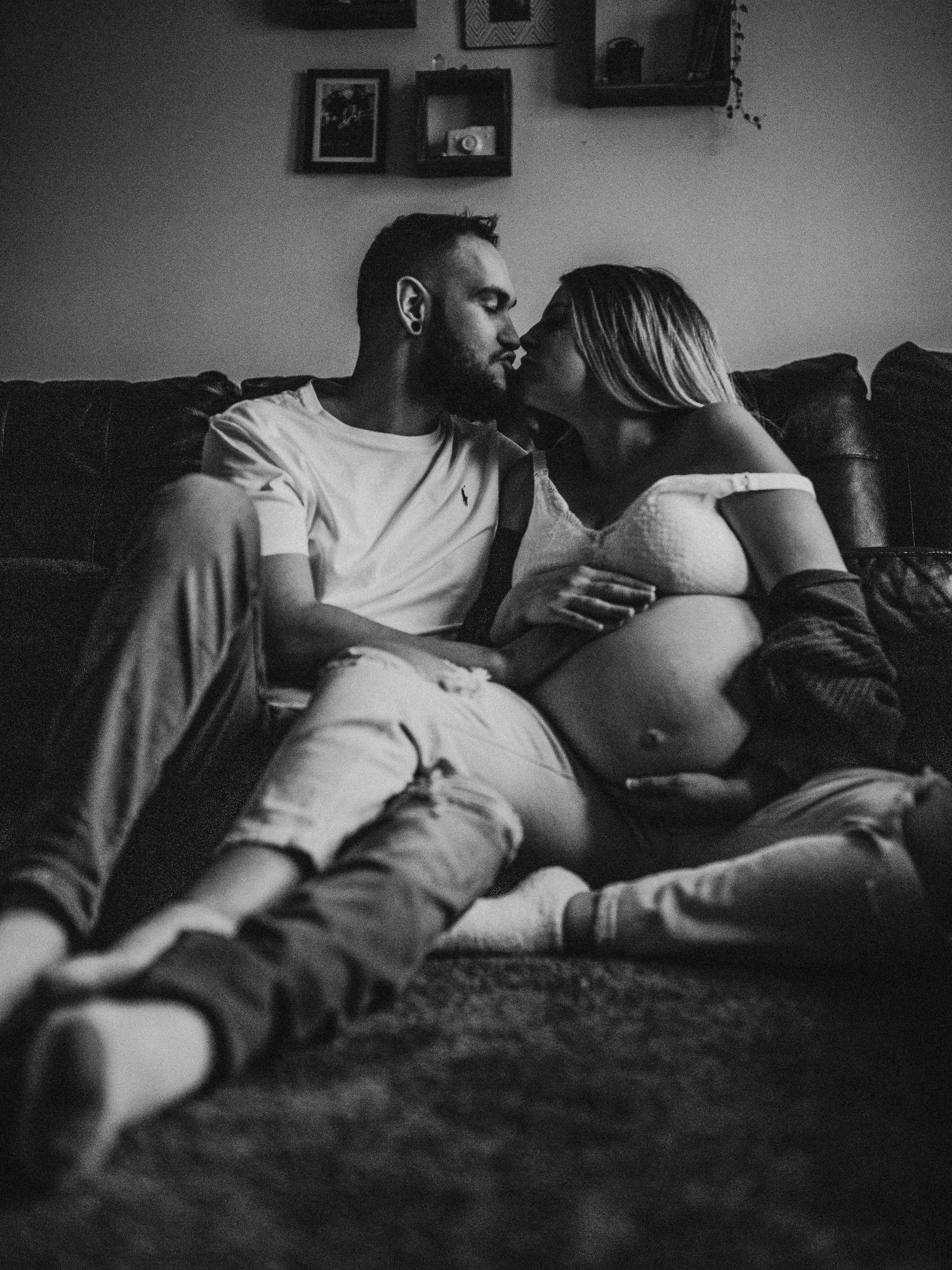 Moody black and white photo of couple resting on couch during maternity photoshoot.