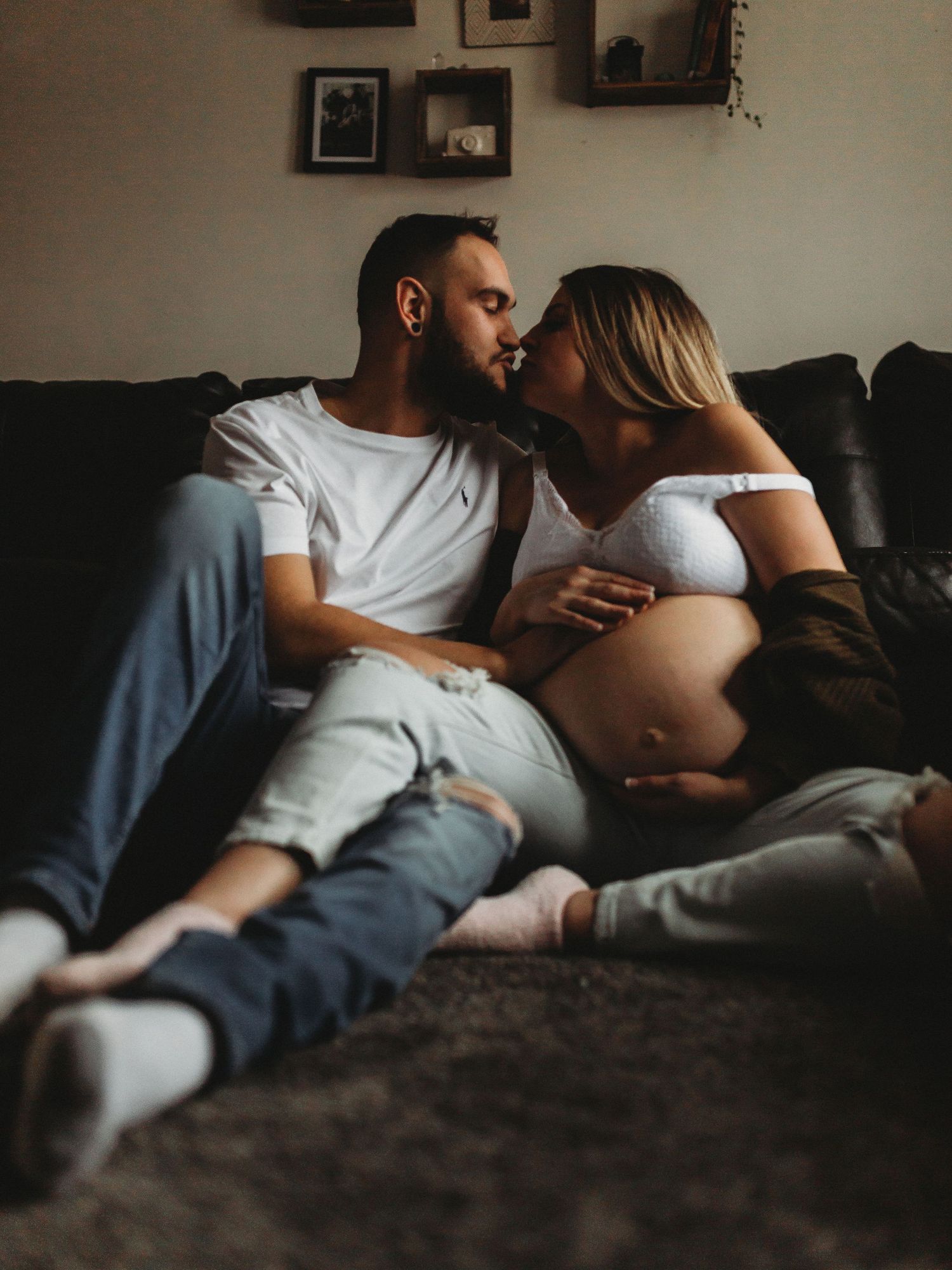 Couple in casual attire sharing intimate moment on couch during pregnancy photoshoot.