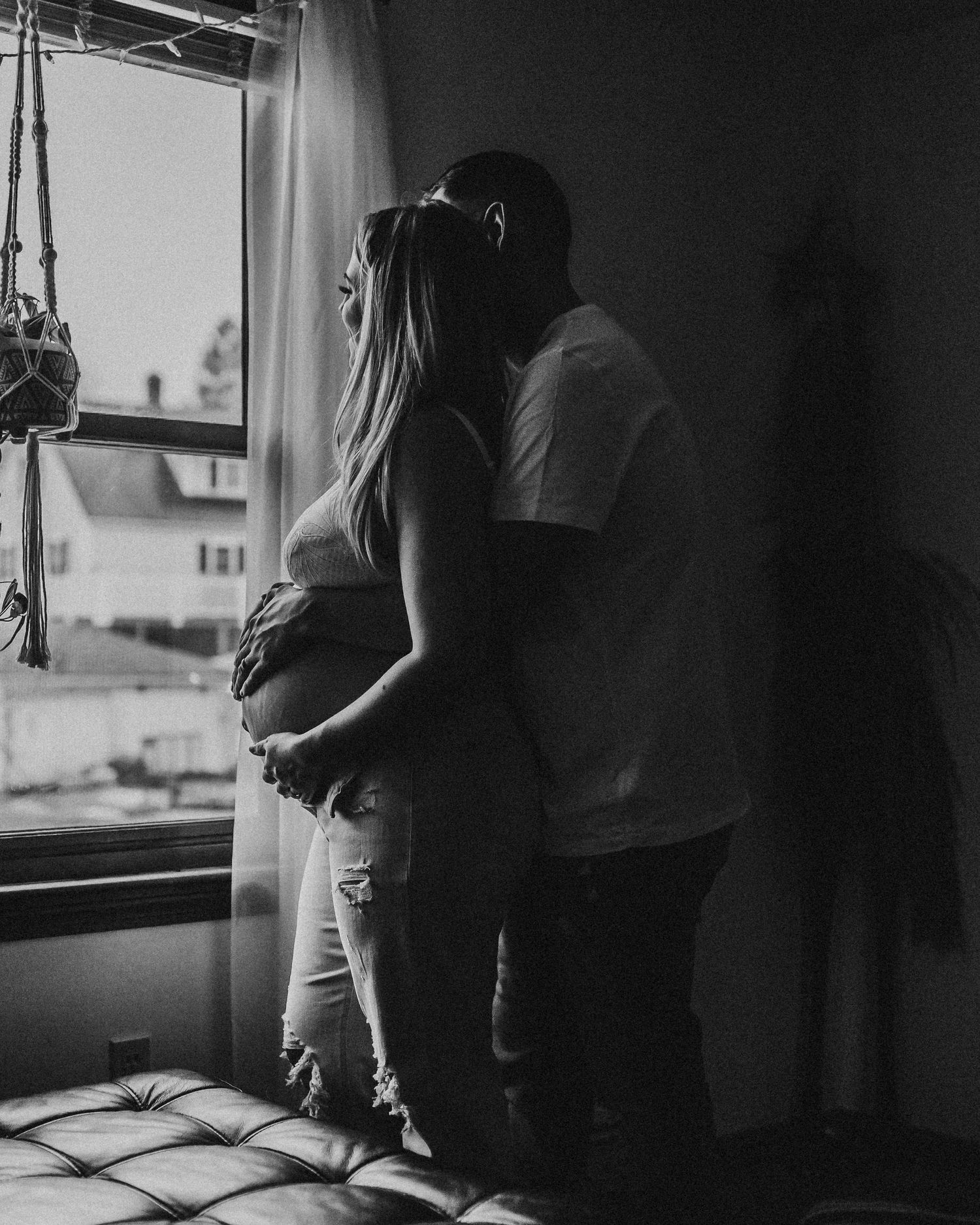 Silhouette of couple standing by window during intimate maternity moment.