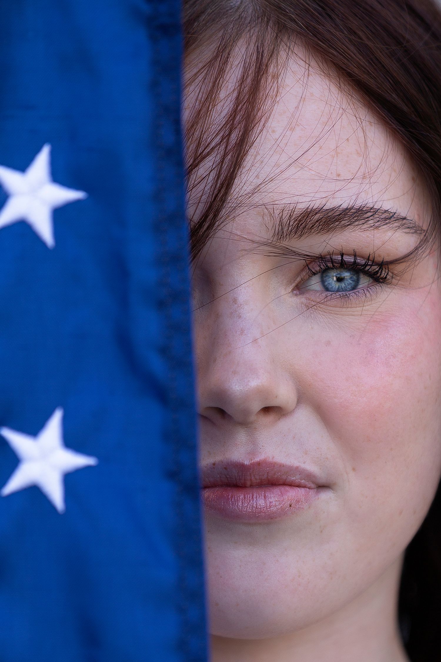 up close of girl blue eye with American flag covering other side of face
