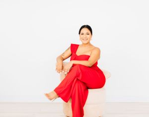 Woman in elegant red dress poses against white backdrop with confident smile.