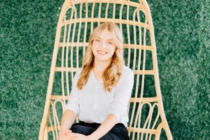 Person relaxing in a rattan hanging chair with green foliage background.