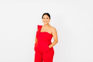 Woman in red one-shoulder dress strikes dynamic pose against white background.