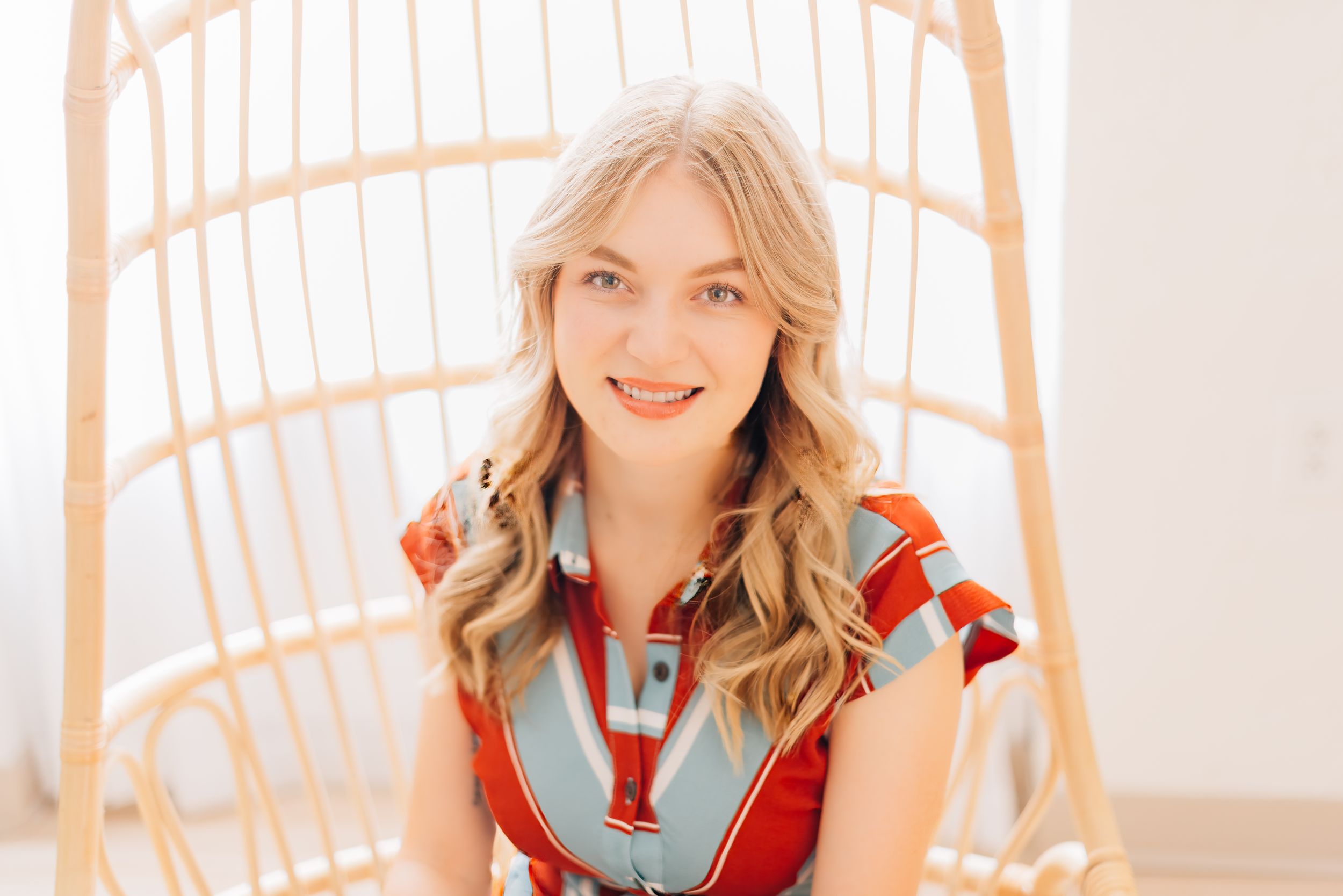 Person sitting comfortably in a suspended rattan chair against neutral background.