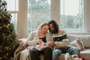 A family shares intimate moments with their newborn baby near a decorated Christmas tree.