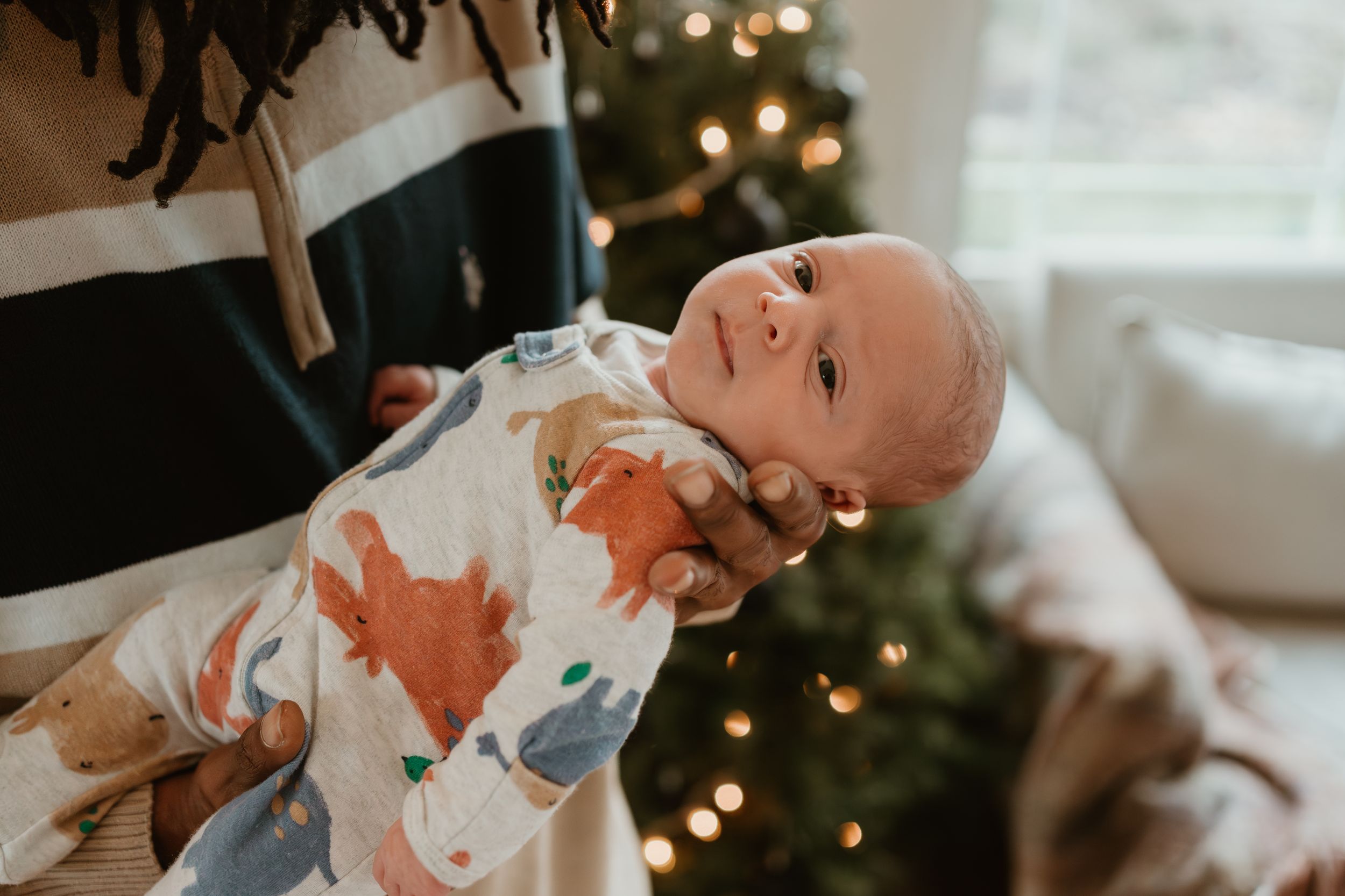 A tender moment between parents and their newborn baby in a cozy room with Christmas lights in the background.