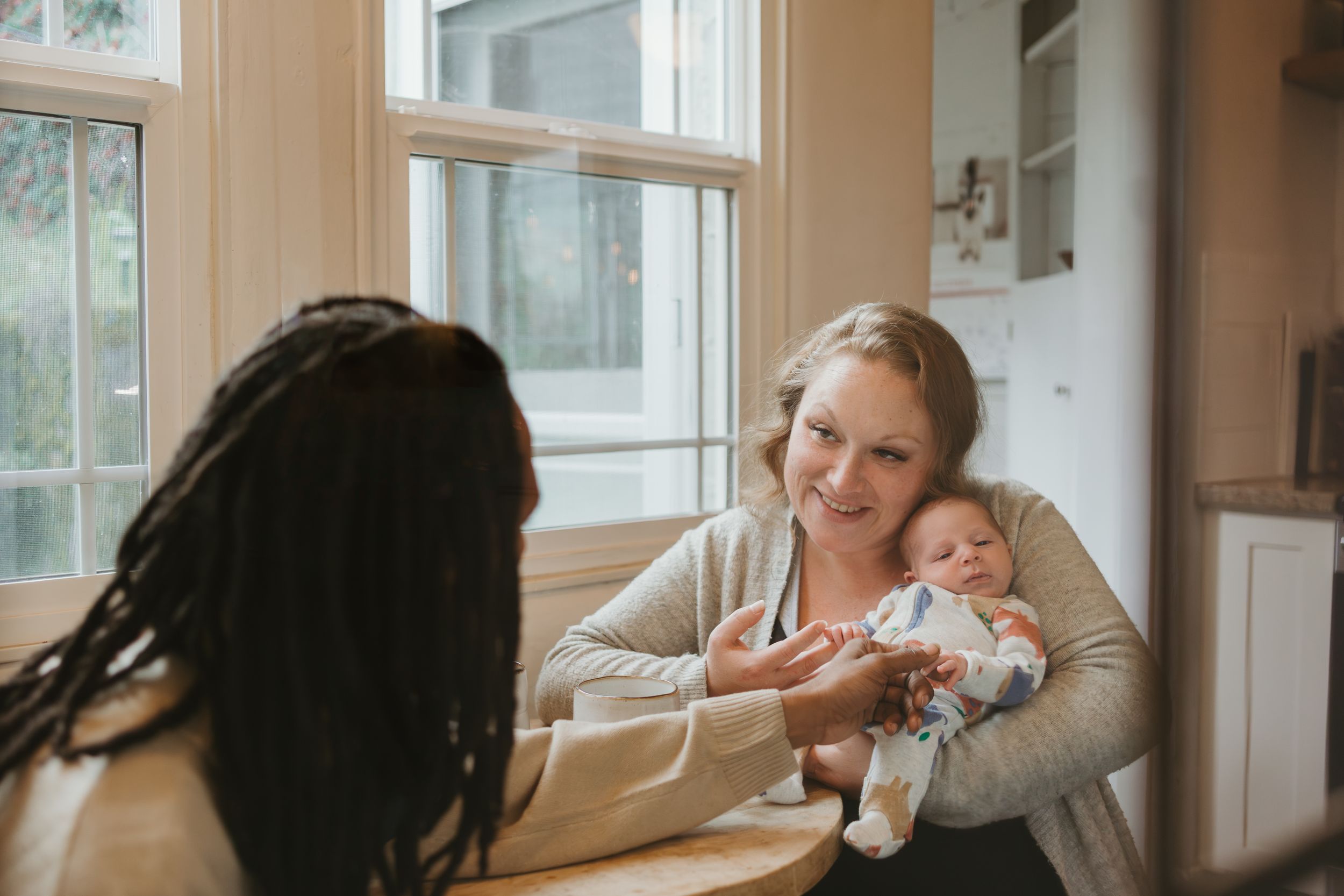 A nurturing scene of feeding a newborn baby by the window in a bright, sunlit room.