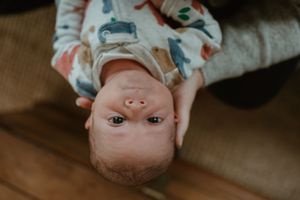 Baby lying on brown surface looking upward with playful expression wearing patterned outfit.