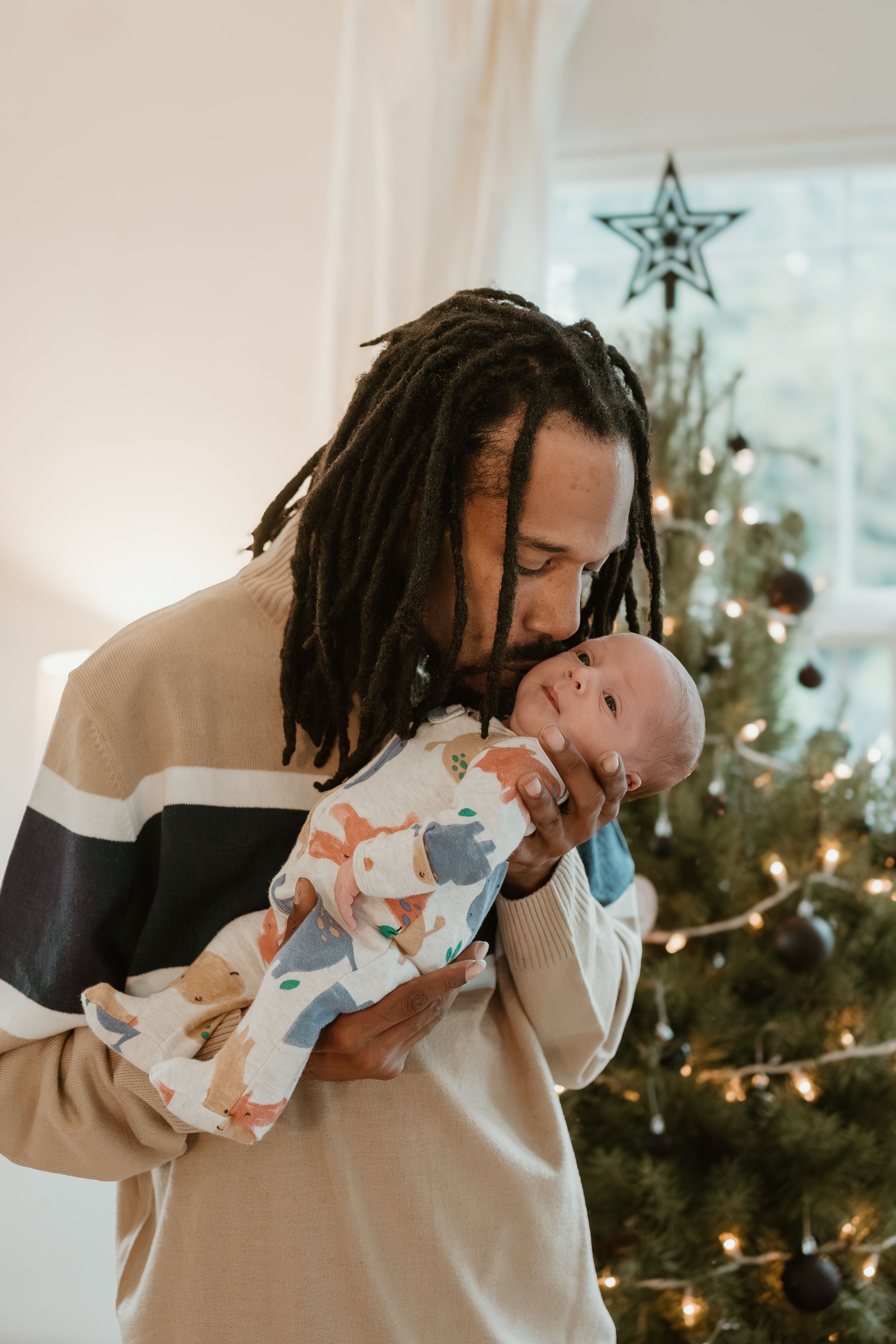 A tender moment between parent and baby near a decorated Christmas tree with star topper.